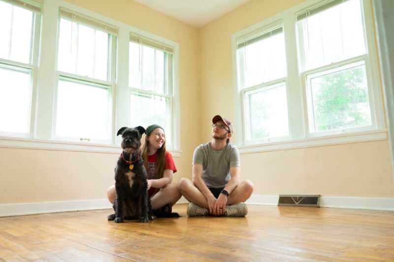 Two people and a dog sitting in a empty room in their new home - make sure you know who to contact when you move