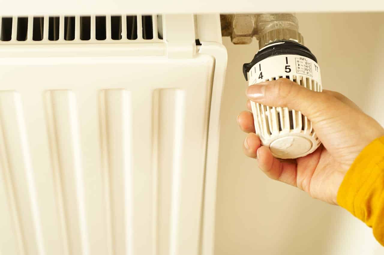 A white person in a yellow jumper adjusts a radiator - could installing a new boiler save you money on your heating bills?