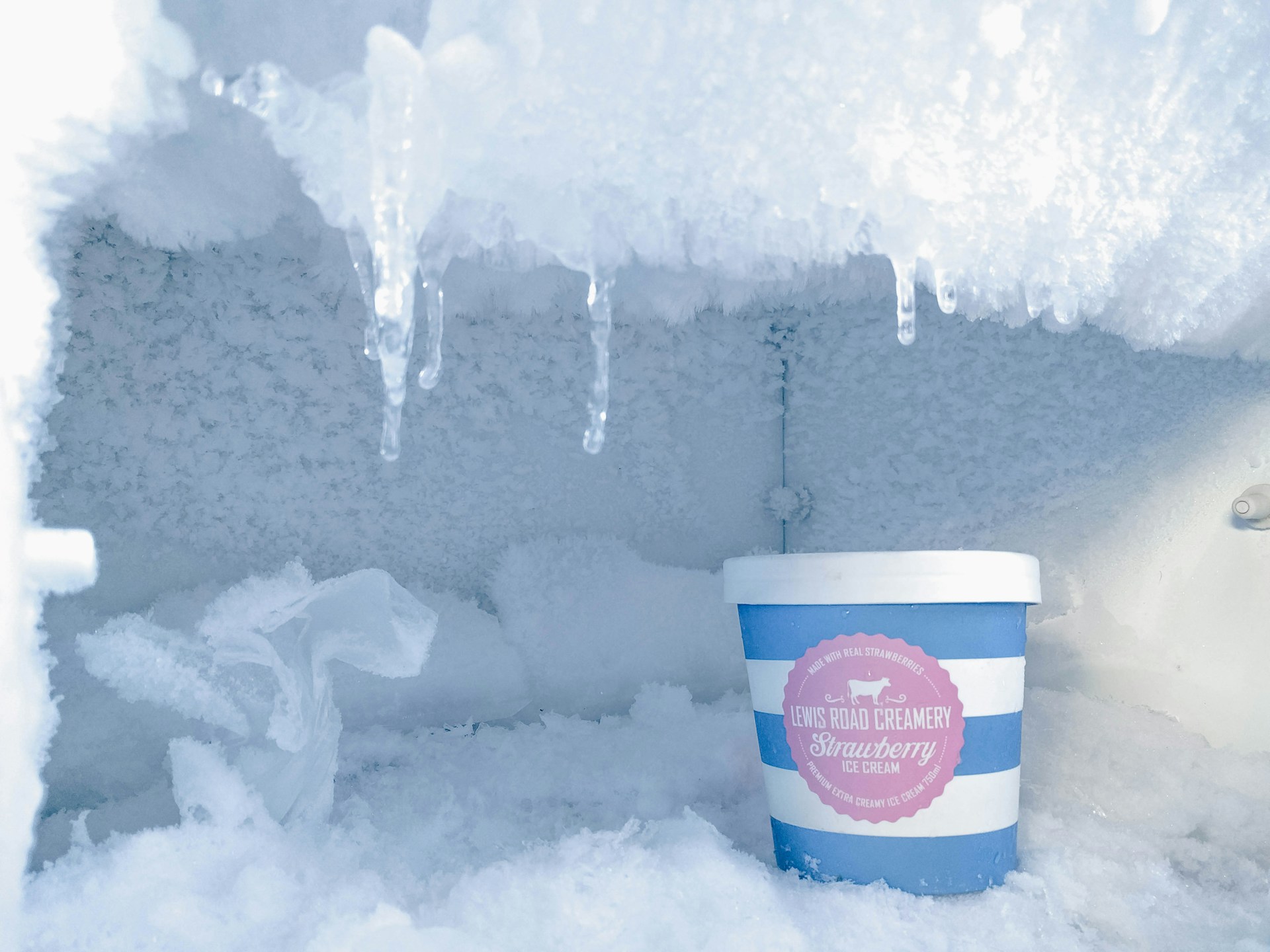 A freezer with ice built up inside and a tub of ice cream. Use our guide to learn how to defrost a freezer quickly and safely.