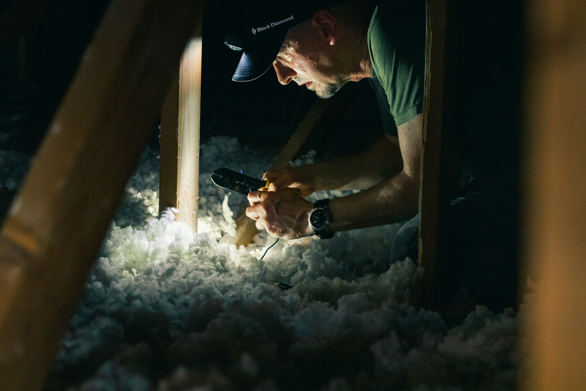 A man using a head torch inspects insulation in an attic.